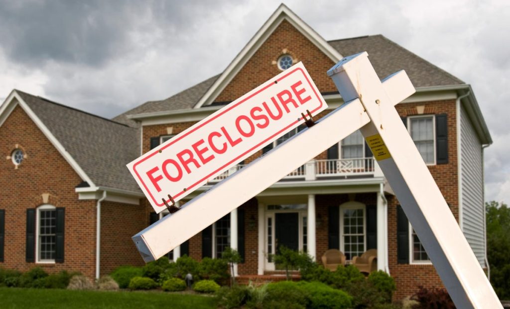 Distressed home being foreclosed on, bent sign in front of home reads, "Foreclosure". 